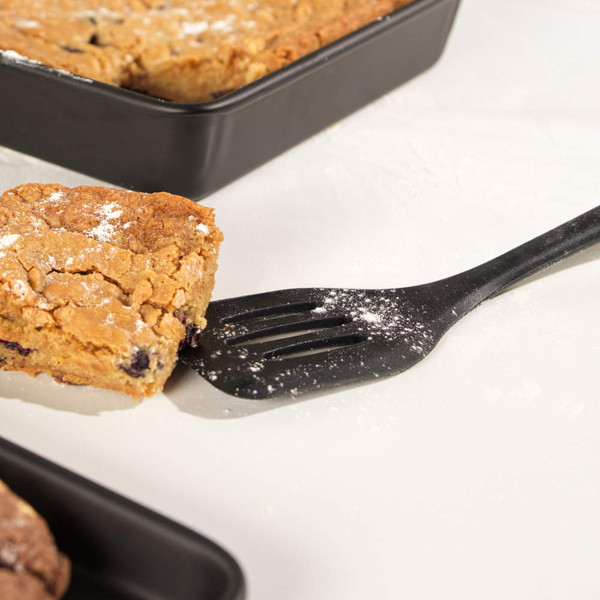 Non-stick black slotted spatula lifting a slice of baked blondie from baking tray