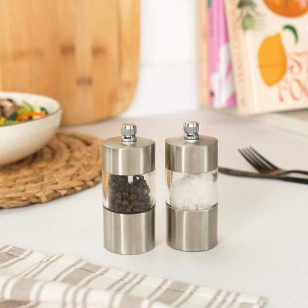 Hand holding stainless steel pepper grinder filled with whole black peppercorns