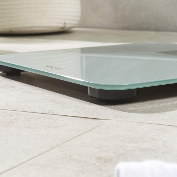 Silver glass digital bathroom scale on tiled floor, close-up side view.