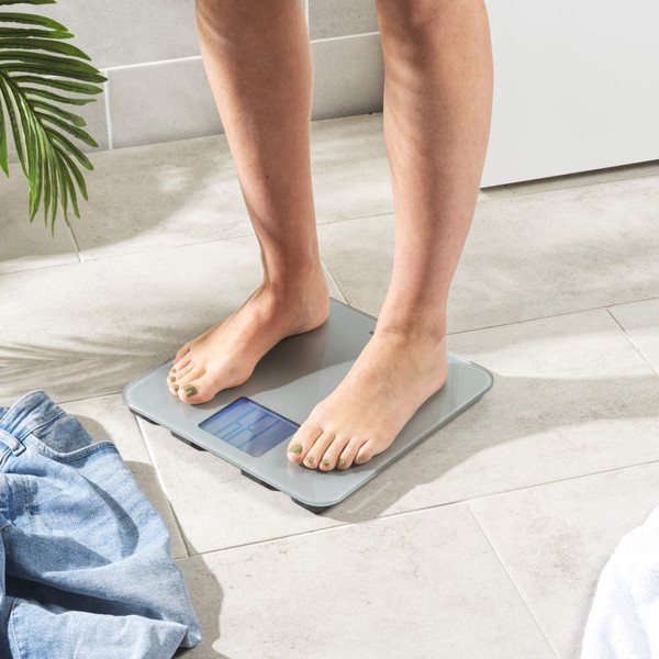 Silver digital bathroom scale with large backlit display, shown at an angle.