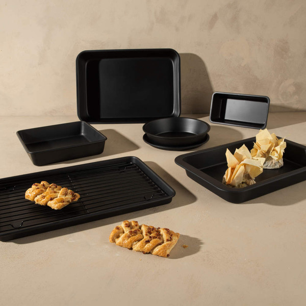 Set of black non-stick baking trays, cake tins and cooling rack on beige surface