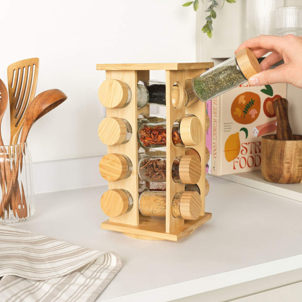 Rotating bamboo spice rack with glass jars on kitchen worktop, hand picking jar