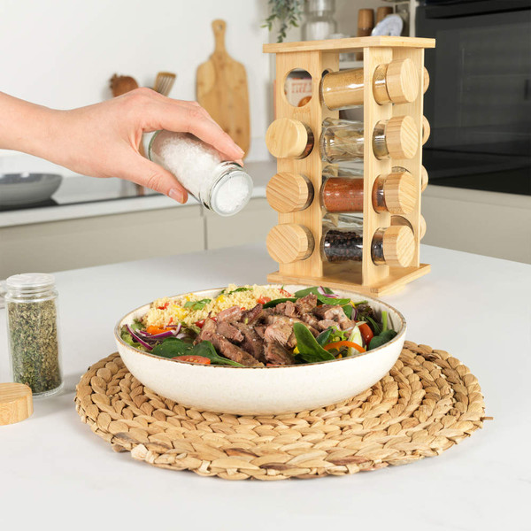 Hand sprinkling salt on salad with grilled beef, beside wooden spice rack in kitchen.