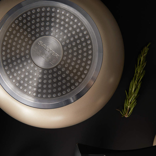 Gold non-stick frying pan base showing induction-compatible surface, partial rosemary sprig