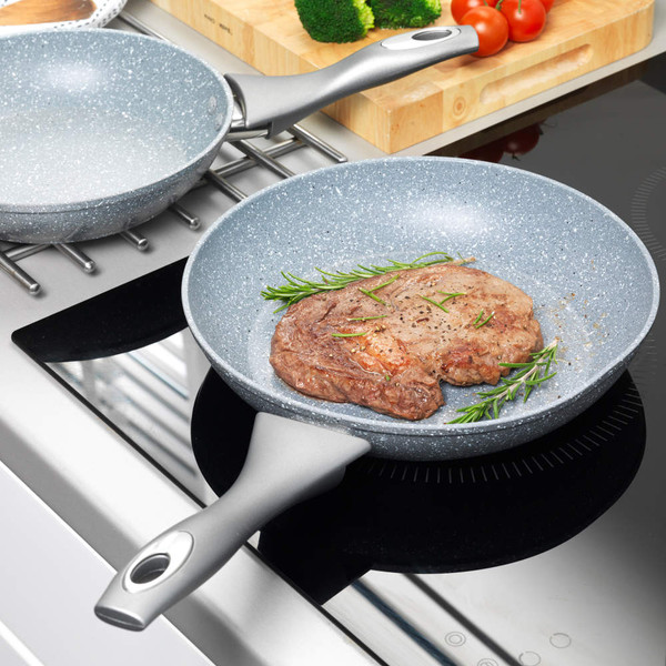 Grey stone-effect frying pan on induction hob with cooked steak and rosemary.