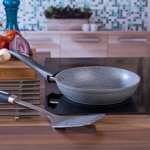 Non-stick grey frying pan on hob with spatula, kitchen background.