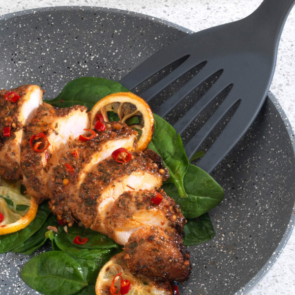 Sliced seasoned chicken breast with chili and lemon on spinach leaves on a dark plate