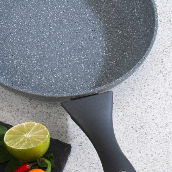 Grey stone-effect non-stick frying pan with black handle on worktop, lime and chillies beside
