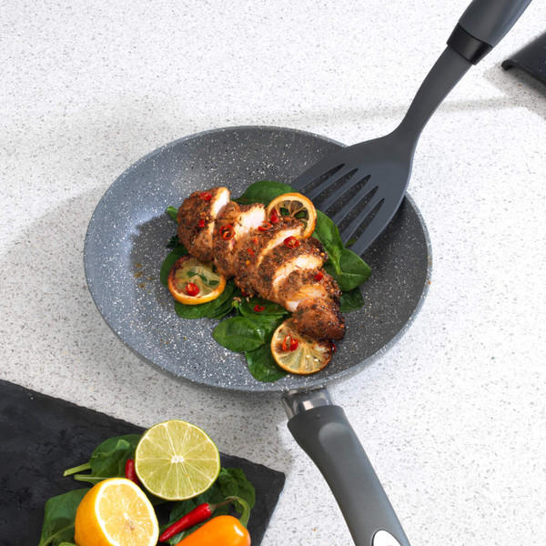 Non-stick frying pan with sliced cooked chicken, lemon and spinach, shown on a kitchen counter