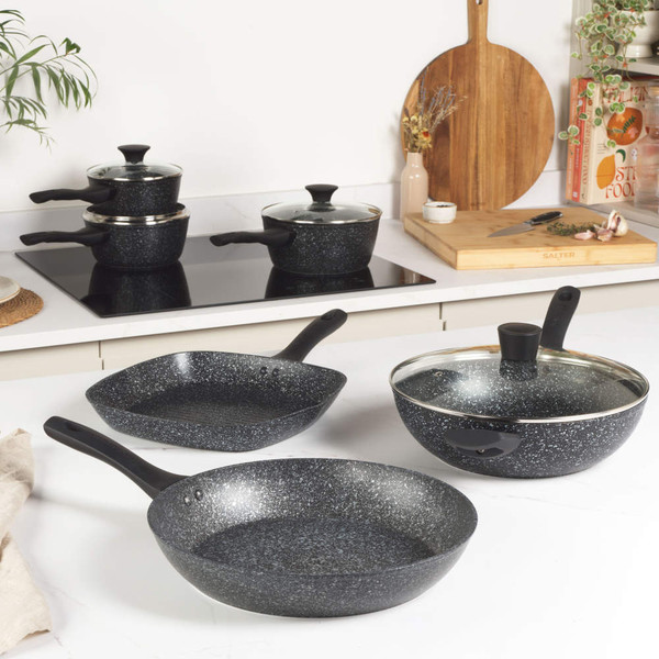 Set of black and white non-stick pans and pots with food on a kitchen worktop