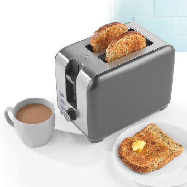 Stainless steel 2-slice toaster with seeded bread, next to cup of tea and buttered toast.