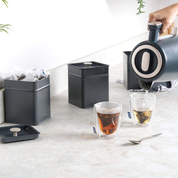 Grey metal tin with lid off, filled with tea bags, on marble worktop