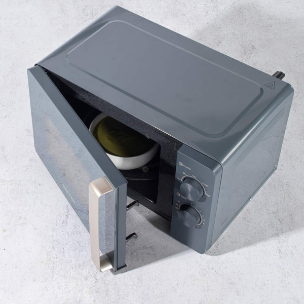 Grey microwave oven with open door showing plate inside, angled top view
