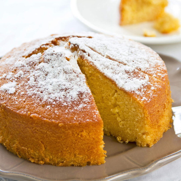 Round sponge cake dusted with icing sugar, one slice served on plate.