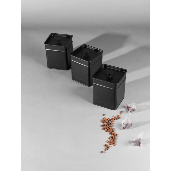 Set of three black metal kitchen storage canisters with coffee beans and tea bags.