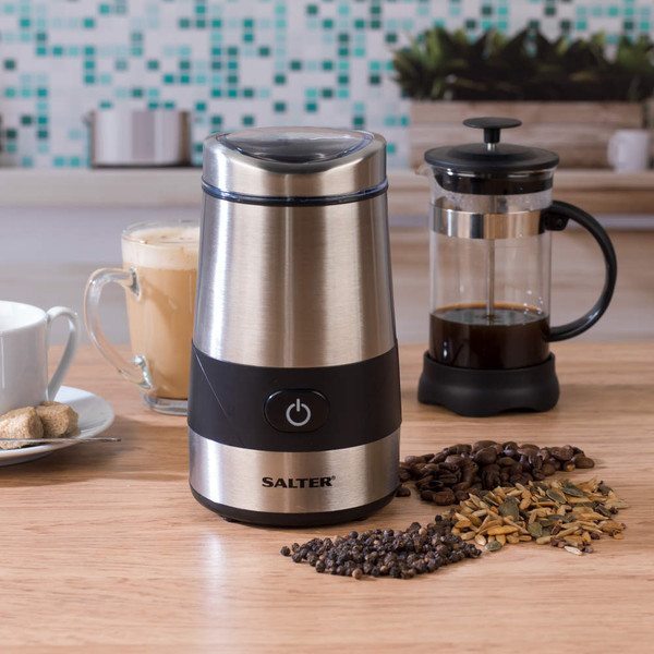Silver electric coffee and spice grinder on kitchen counter with coffee press and ingredients.