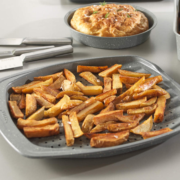 Grey non-stick oven tray with homemade chips, shown with matching bakeware and knives.