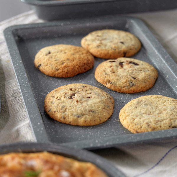 Grey non-stick oven tray with homemade chips, shown with matching bakeware and knives.