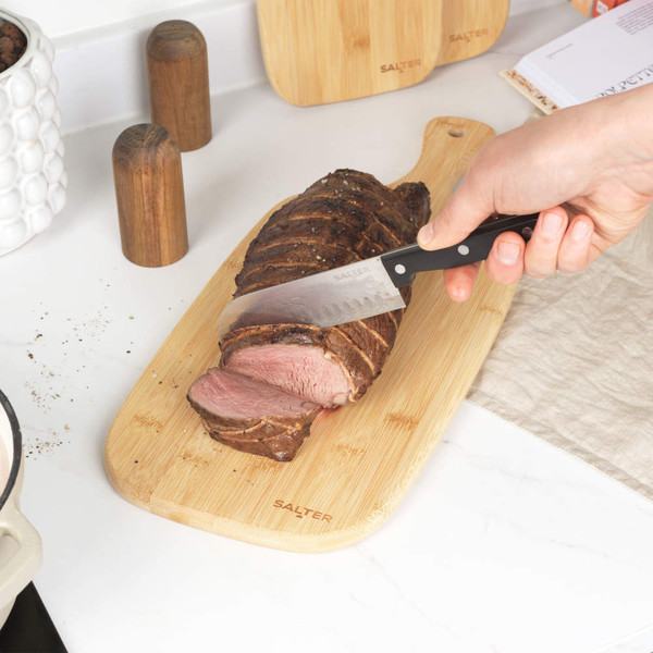 Slicing roast beef on a wooden Salter chopping board in a kitchen.