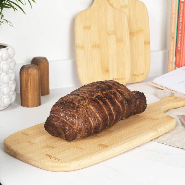 Cooked beef joint on bamboo chopping board in kitchen setting