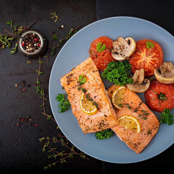 Grilled salmon fillets with lemon, served with roasted tomatoes, mushrooms and herbs on a plate