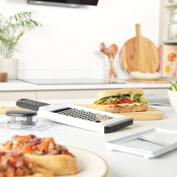 White handheld grater with black handle, shown on kitchen counter beside a vegetable sandwich.
