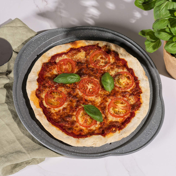 Hand using pizza cutter to slice margherita pizza on grey tray