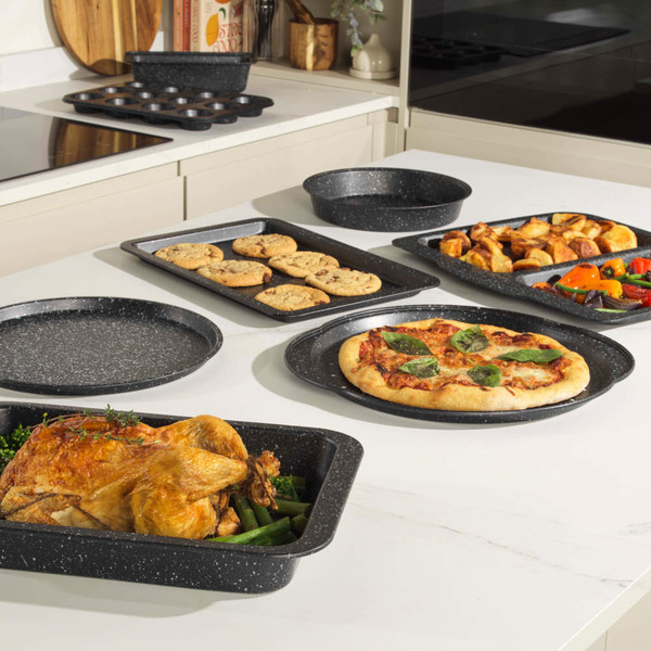 Set of non-stick grey baking trays and dishes with roast chicken, pizza, biscuits and vegetables.