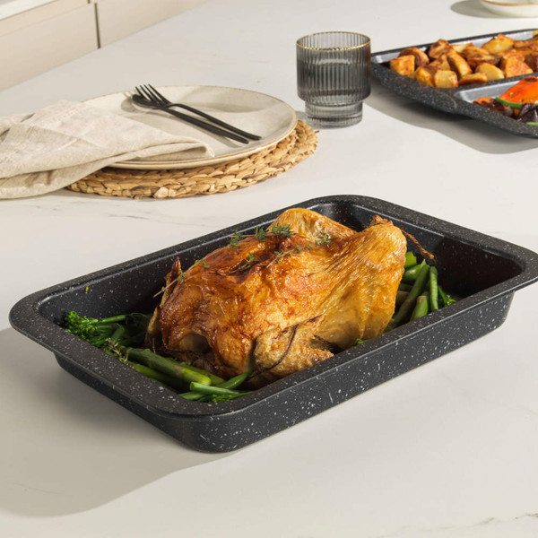 Roast chicken served in a black roasting tin on green vegetables, kitchen table setting