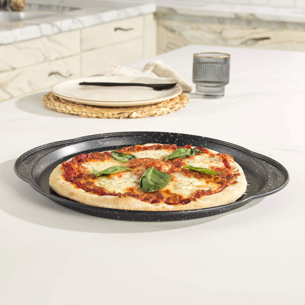 Non-stick round pizza tray with Margherita pizza, shown on a light kitchen counter.