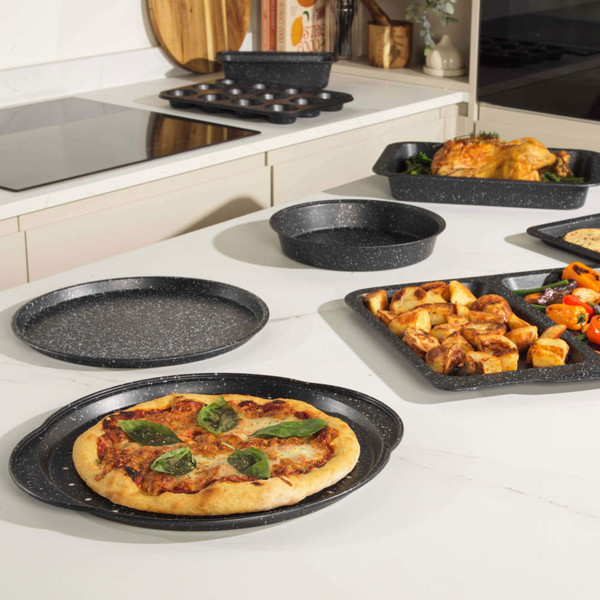 Set of grey non-stick oven trays and bakeware with pizza, roast chicken, vegetables and cookies displayed on a kitchen counter