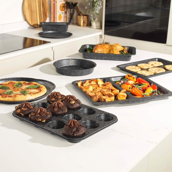 Black speckled non-stick bakeware set displayed on kitchen counter, showing pizza tray, muffin tray, roasting pans and cookie tray.