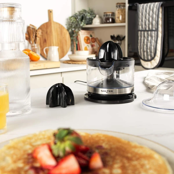 Black and silver electric citrus juicer with clear jug and handle, shown from front.