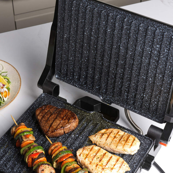 Electric grill with grilled chicken fillets, steak and vegetable skewers on cooking surface