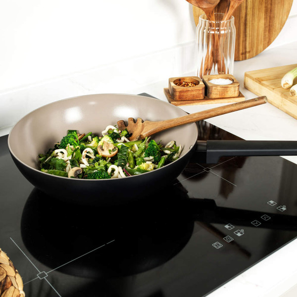 Non-stick frying pan on induction hob with stir-fried vegetables and wooden spatula