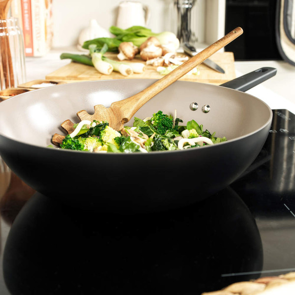 Black non-stick wok with stir-fry vegetables and wooden spatula on hob