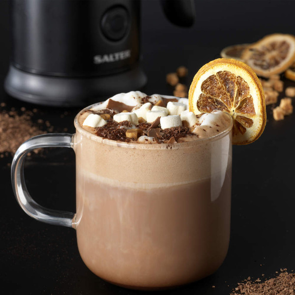 Glass mug of hot chocolate topped with marshmallows, chocolate shavings, and dried orange slice.