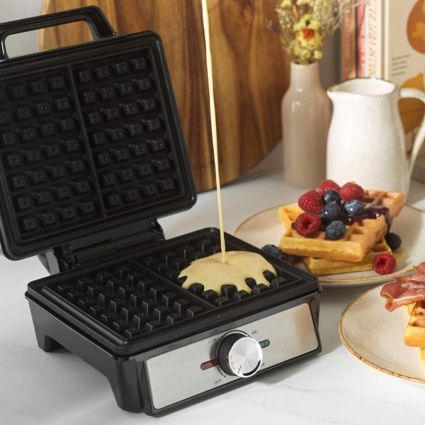 Black waffle maker with two golden waffles, lid open, showing temperature dial