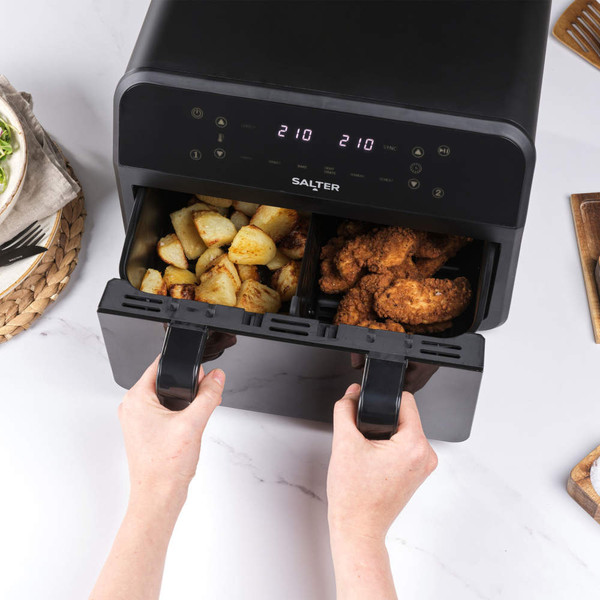 Black dual drawer air fryer with roast potatoes and breaded chicken inside, shown in use on kitchen worktop
