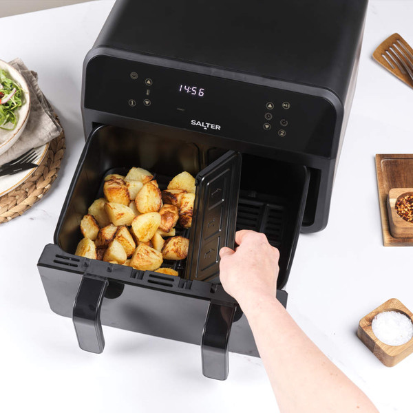 Black dual drawer air fryer with roast potatoes and breaded chicken inside, shown in use on kitchen worktop