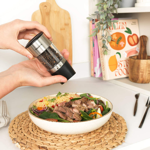 SALTER stainless steel pepper mill in use, seasoning salad and steak on kitchen table.
