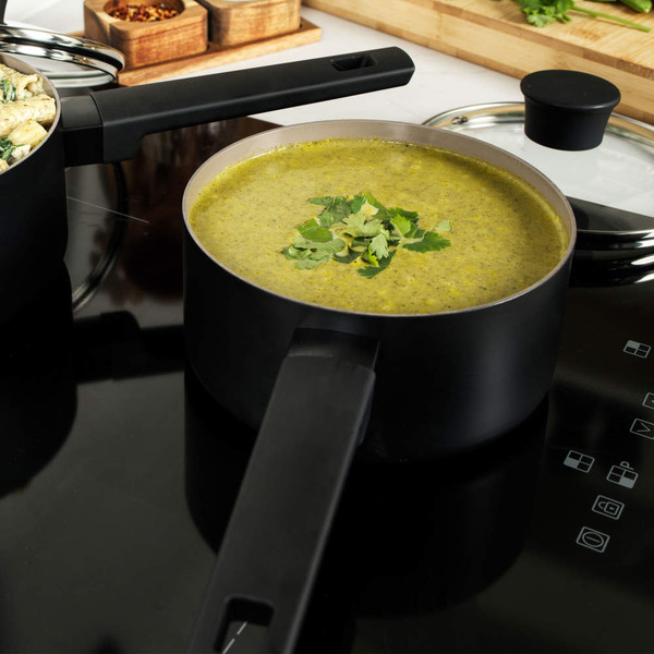 Black saucepan with green vegetable soup on induction hob, garnished with fresh herbs.