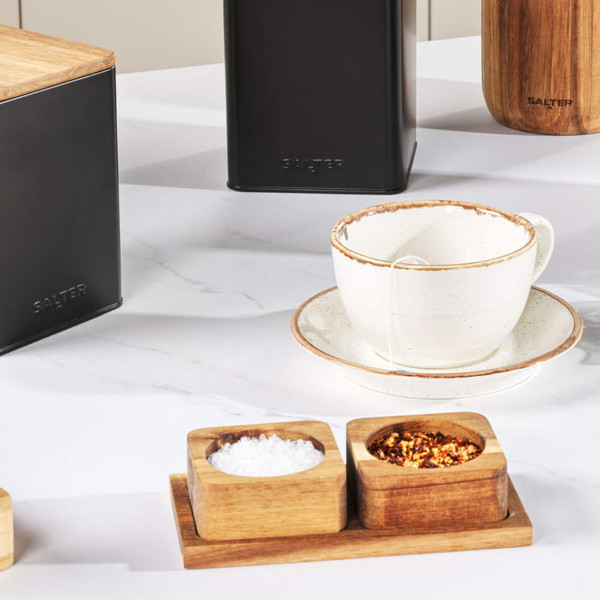 Black metal storage canisters and wooden spice pots on white kitchen counter with mug
