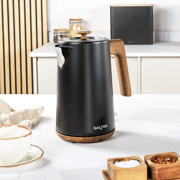 Matte black electric kettle pouring hot water into cup, shown on kitchen worktop.