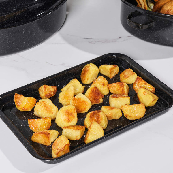 Black enamel roasting pan and tray set on kitchen counter with cooked roast and vegetables