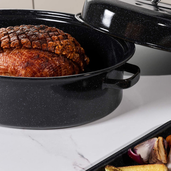 Roast joint in a black speckled enamel roasting pan with lid, shown on a kitchen counter.