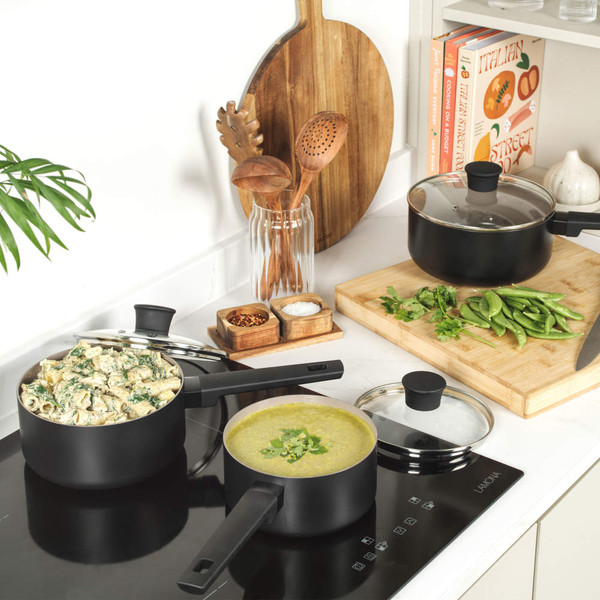 Set of black saucepans with food on hob, shown in modern kitchen setting