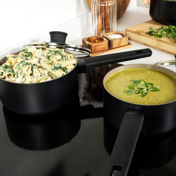 Two black saucepans on hob, one with creamy pasta, one with green soup