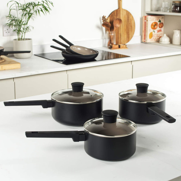 Set of three black non-stick saucepans with lids on kitchen worktop