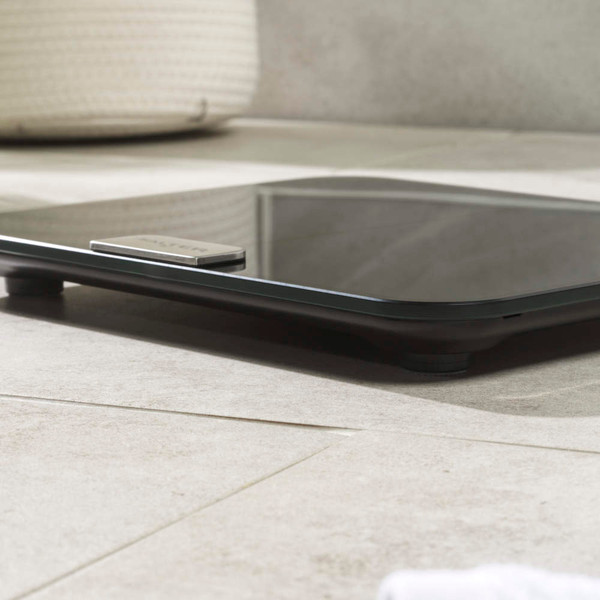 Black glass digital bathroom scale on tiled floor, side view